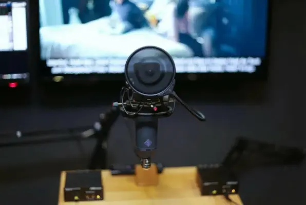 Professional Neumann condenser microphone with pop filter in the recording booth at SOUNDSTARSTUDIOS Munich; background monitor shown for video podcasts and dubbing sessions.